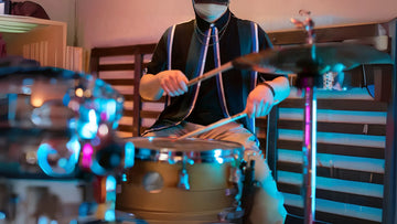 Masked drummer playing indoor kit with lights